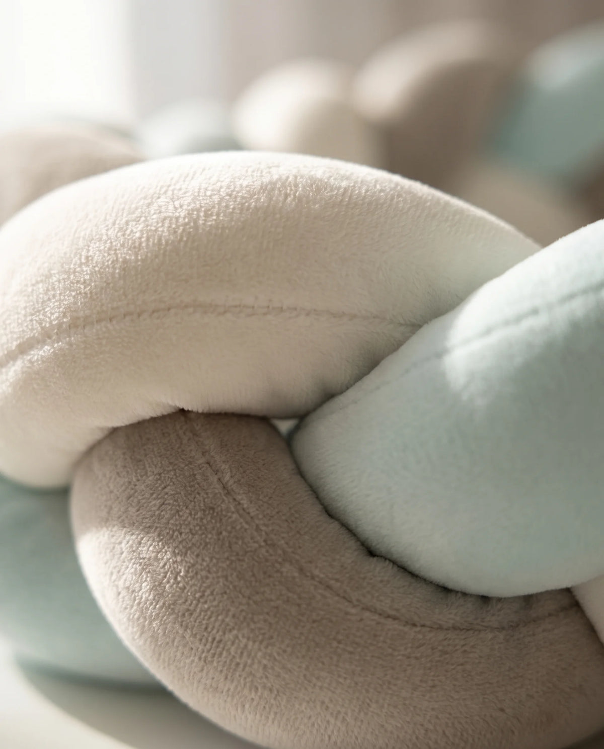 Gros plan sur la texture velours d'un tour de lit tressé bébé aux brins écru, taupe et bleu ciel finement cousus.