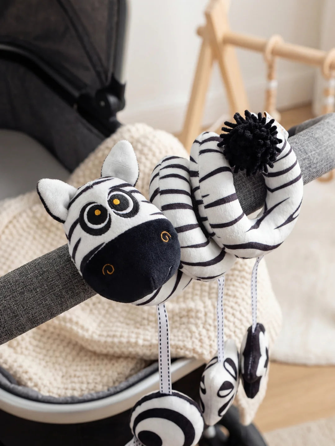 Spirale d'éveil zèbre en peluche fixée sur la poignée d'une poussette pour les sorties.