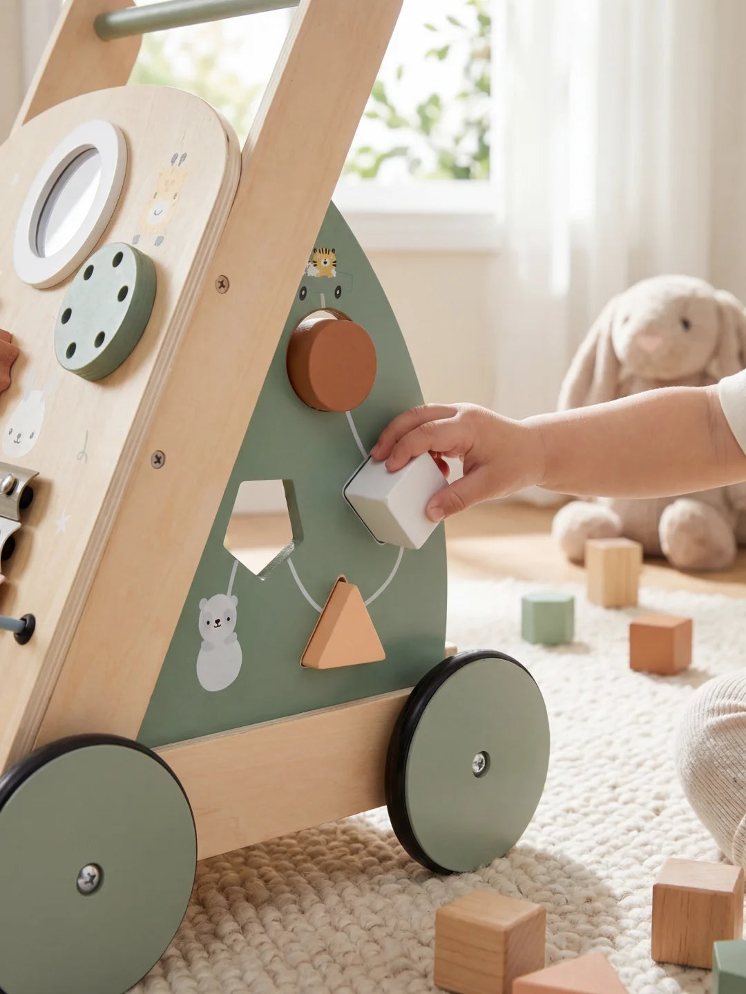 Main d'un enfant insérant un cube en bois dans le trieur de formes d'un chariot de marche.