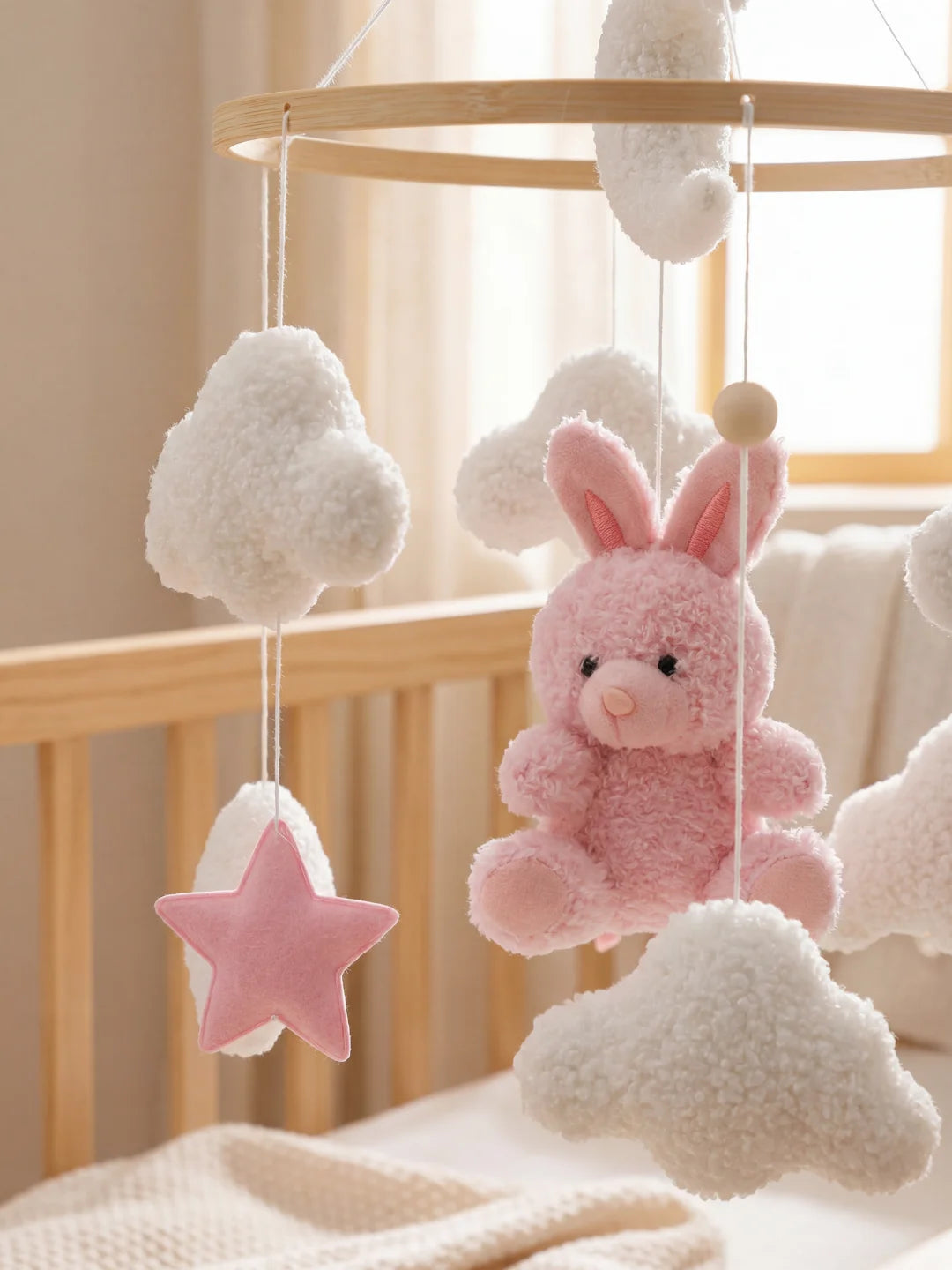 Détail rapproché de la peluche lapin rose et des nuages moutonneux d'un mobile pour bébé.
