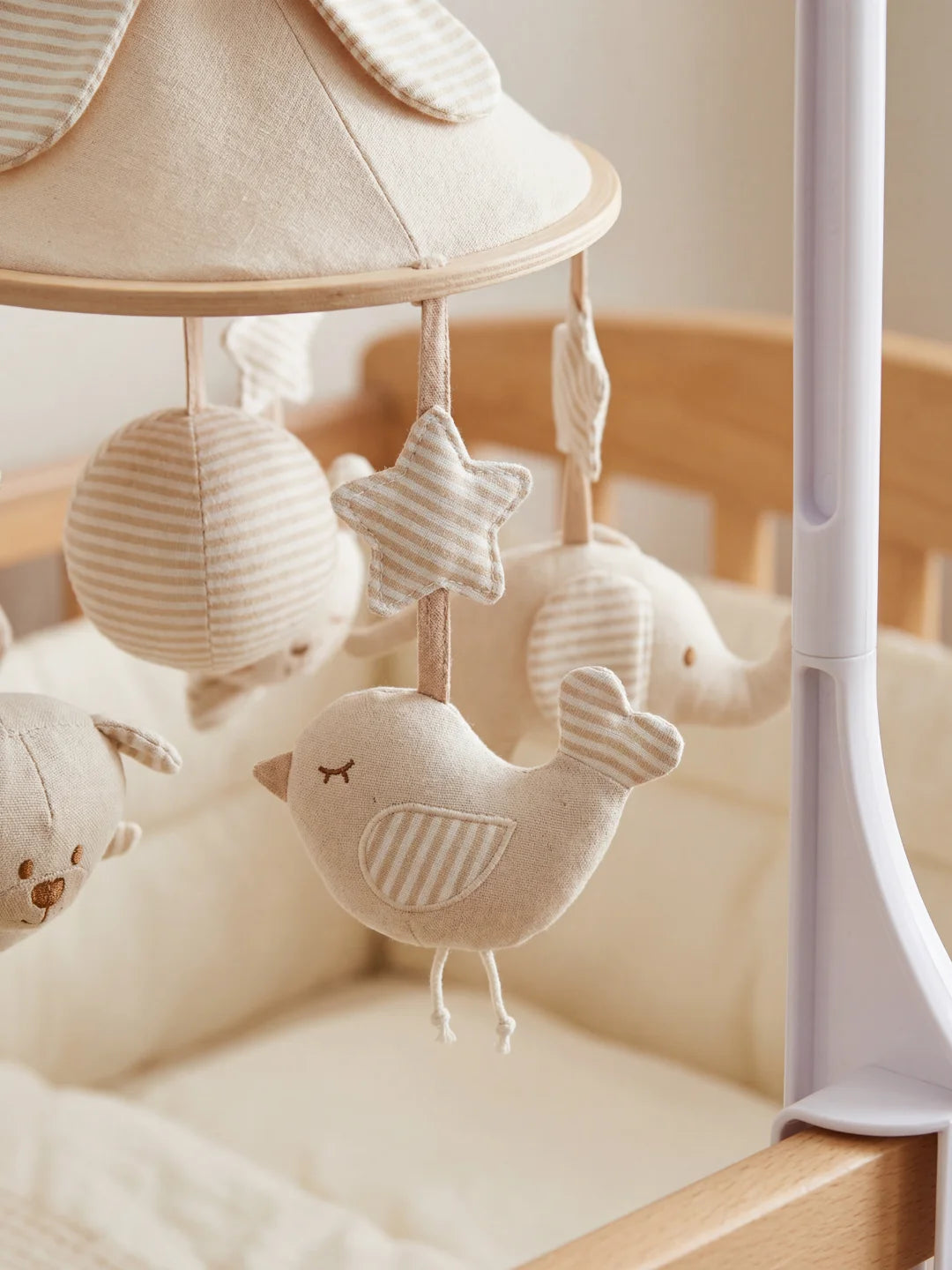 Zoom sur une étoile et un petit oiseau en tissu beige d'un mobile d'éveil pour lit de bébé.