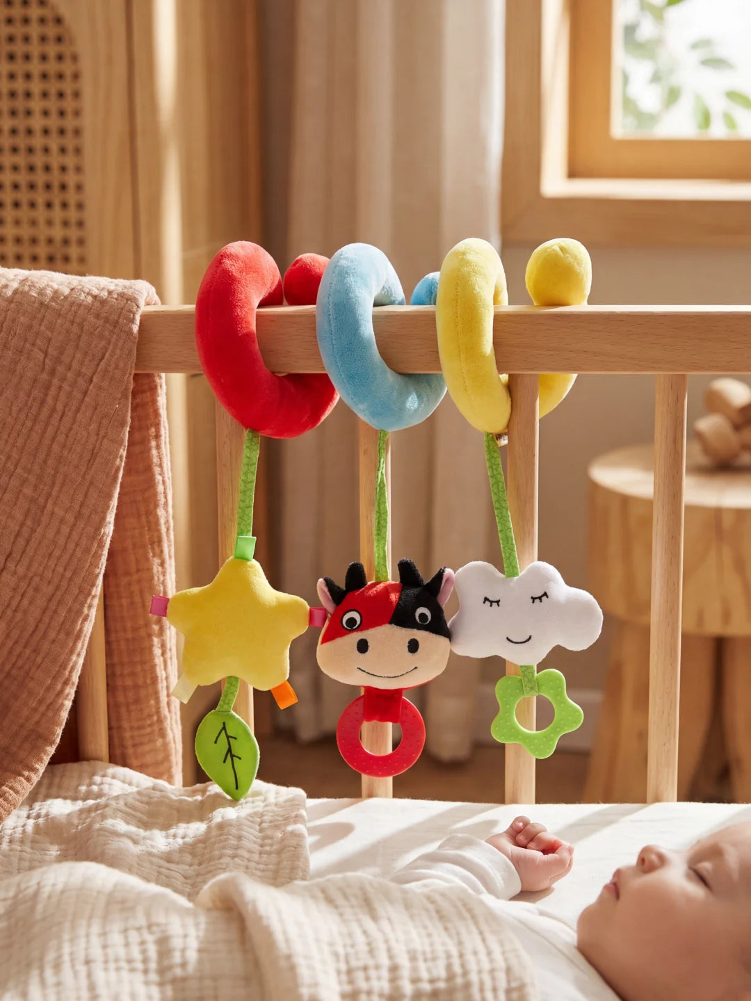 Spirale d'éveil colorée fixée sur le bord d'un lit pendant que bébé fait la sieste en arrière-plan.