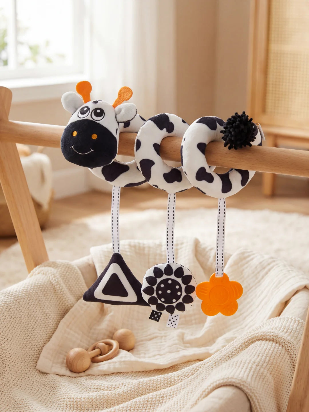 Spirale d'éveil avec hochets géométriques et tête de vachette sur un portique en bois.