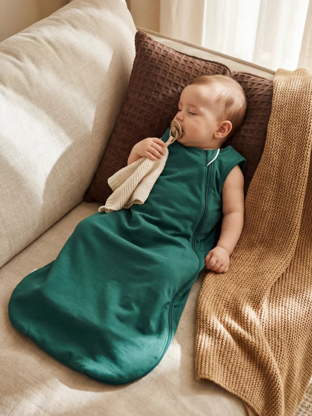Bébé endormi dans sa gigoteuse en jersey vert sapin sur un canapé avec doudou