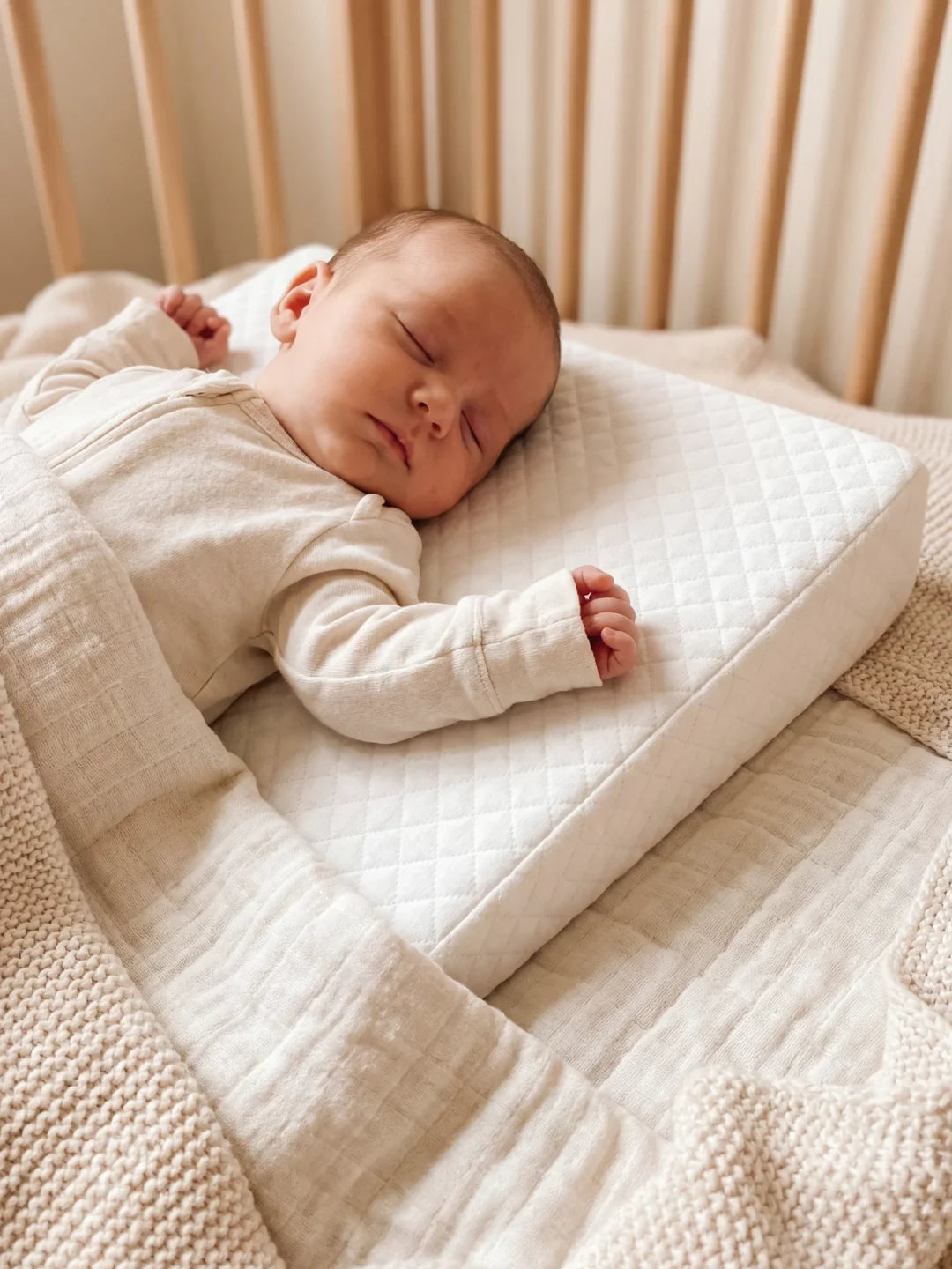 bébé endormi sur un plan incliné anti reflux blanc dans son lit