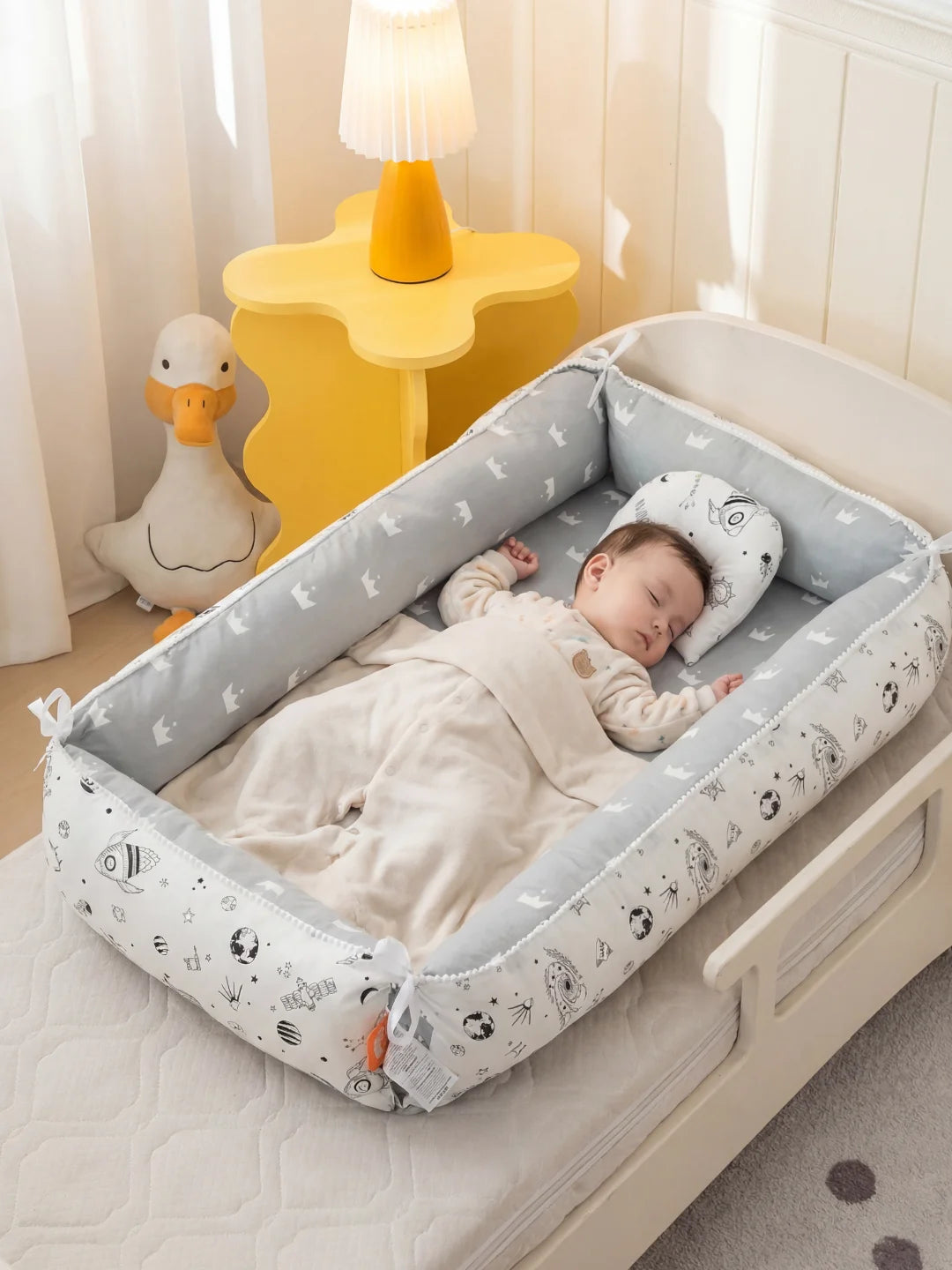Bébé endormi dans un nid d'ange ergonomique gris et blanc avec oreiller de maintien assorti.