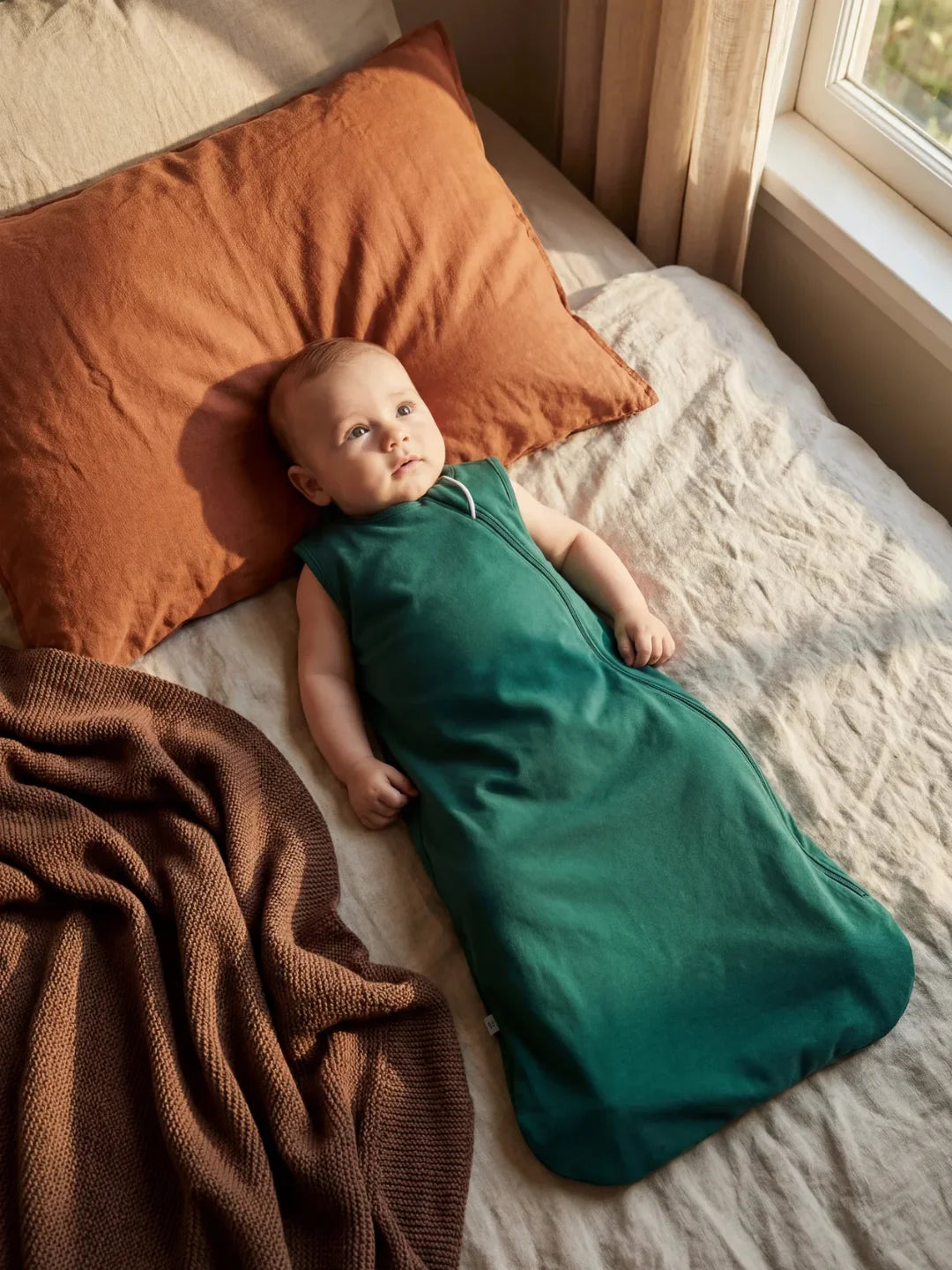 Bébé éveillé allongé dans sa gigoteuse jersey vert sapin sur un lit