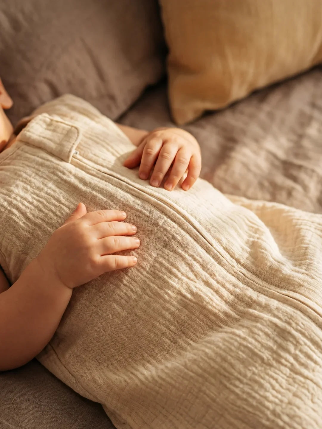 Détail des mains de bébé posées sur sa gigoteuse gaze de coton écru
