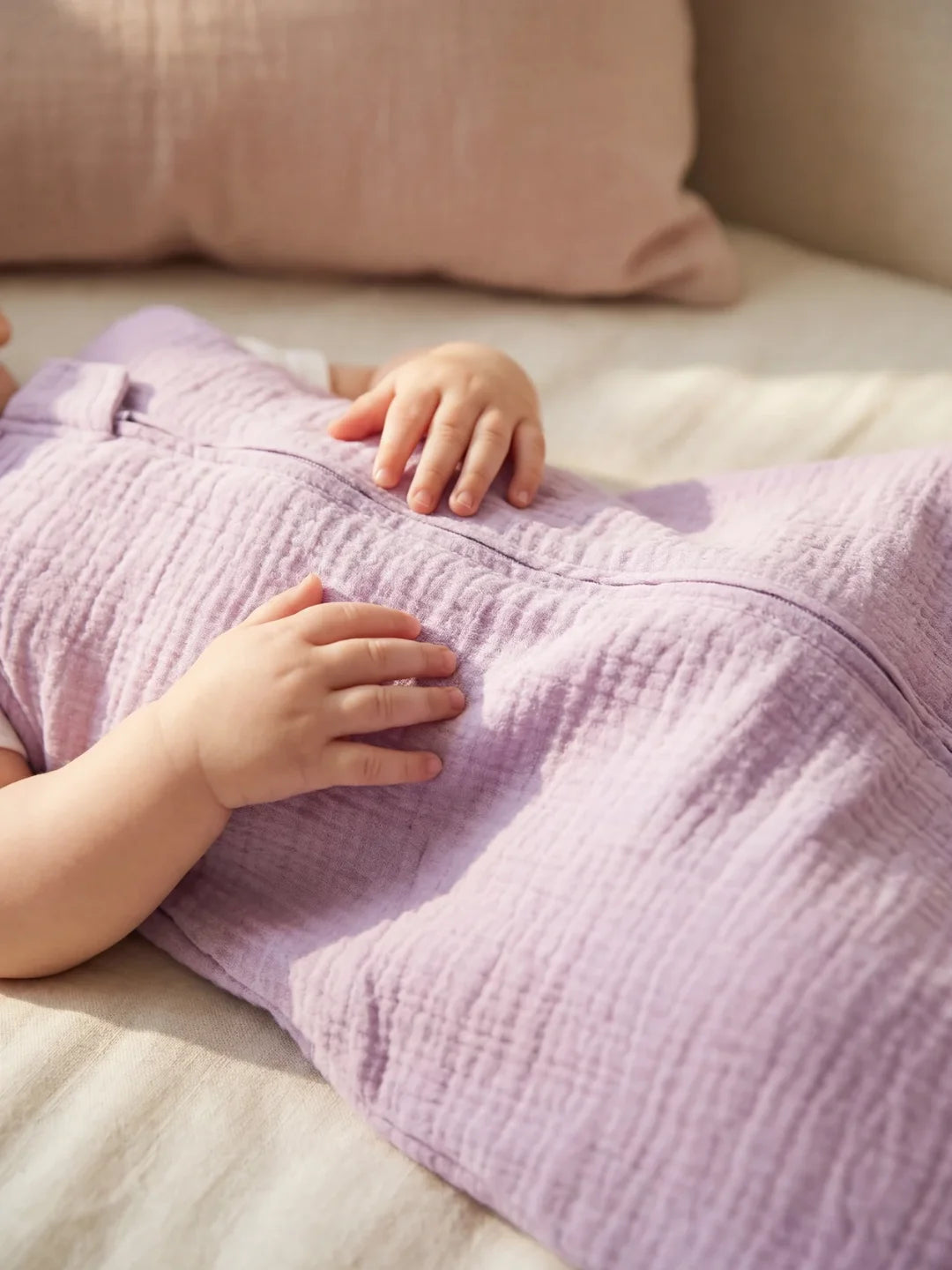 Détail des mains de bébé posées sur sa gigoteuse gaze de coton lavande