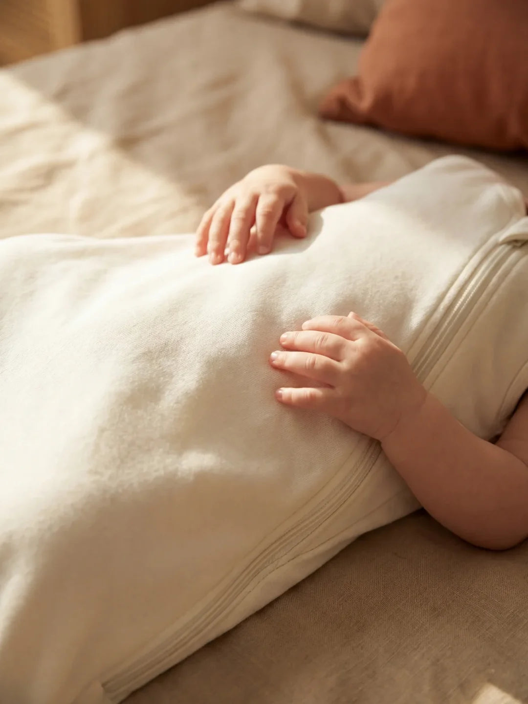 Détail des mains de bébé posées sur sa gigoteuse jersey blanc écru