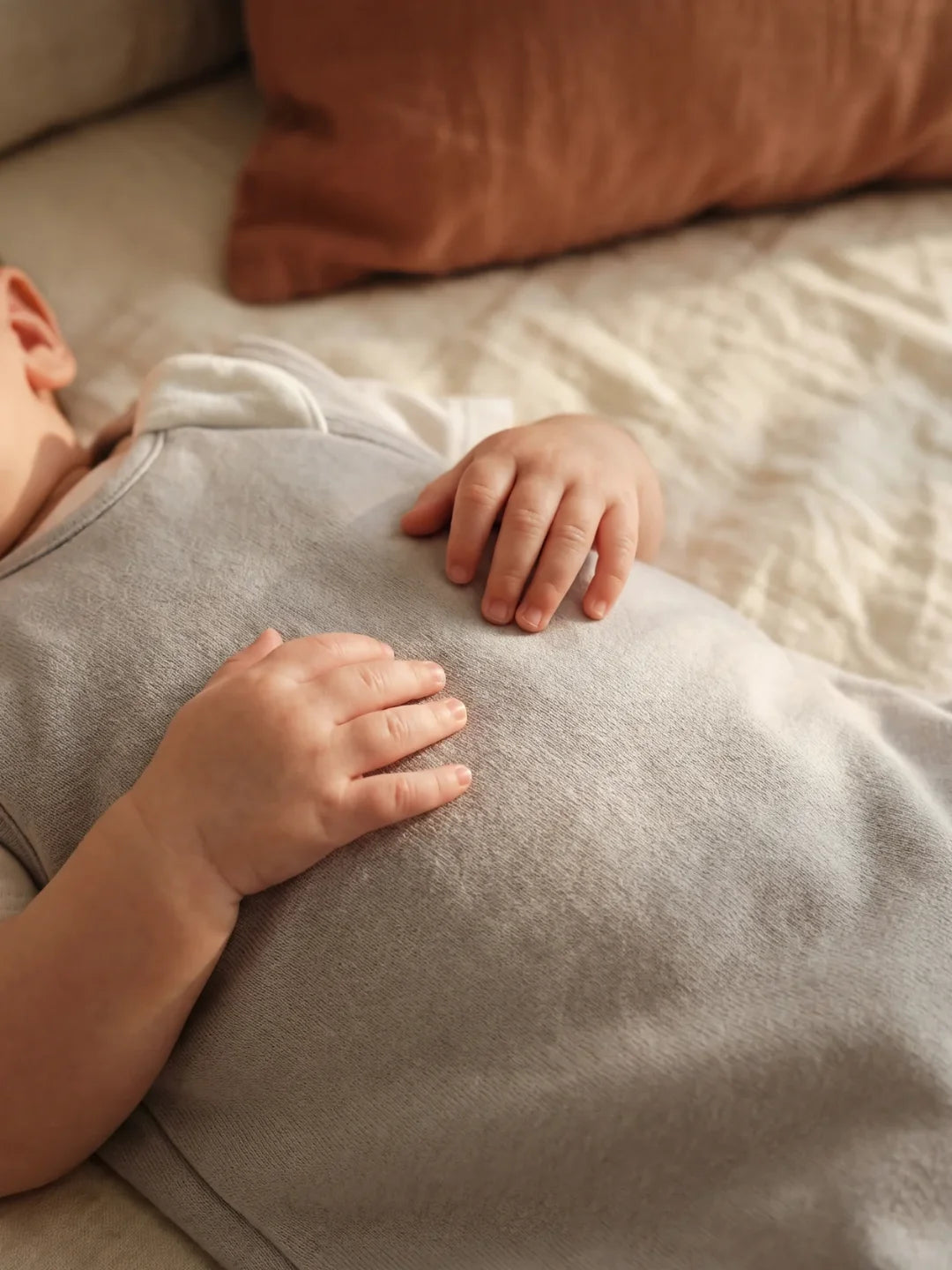 Détail des mains de bébé posées sur sa gigoteuse jersey gris clair