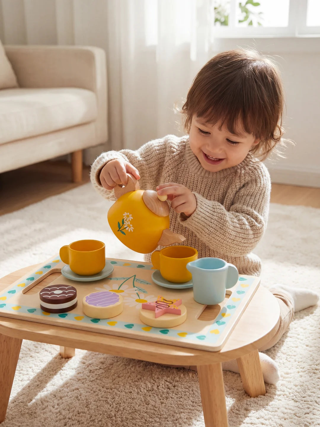 Bébé manipulant une théière jaune et des tasses colorées en bois sur un tapis blanc