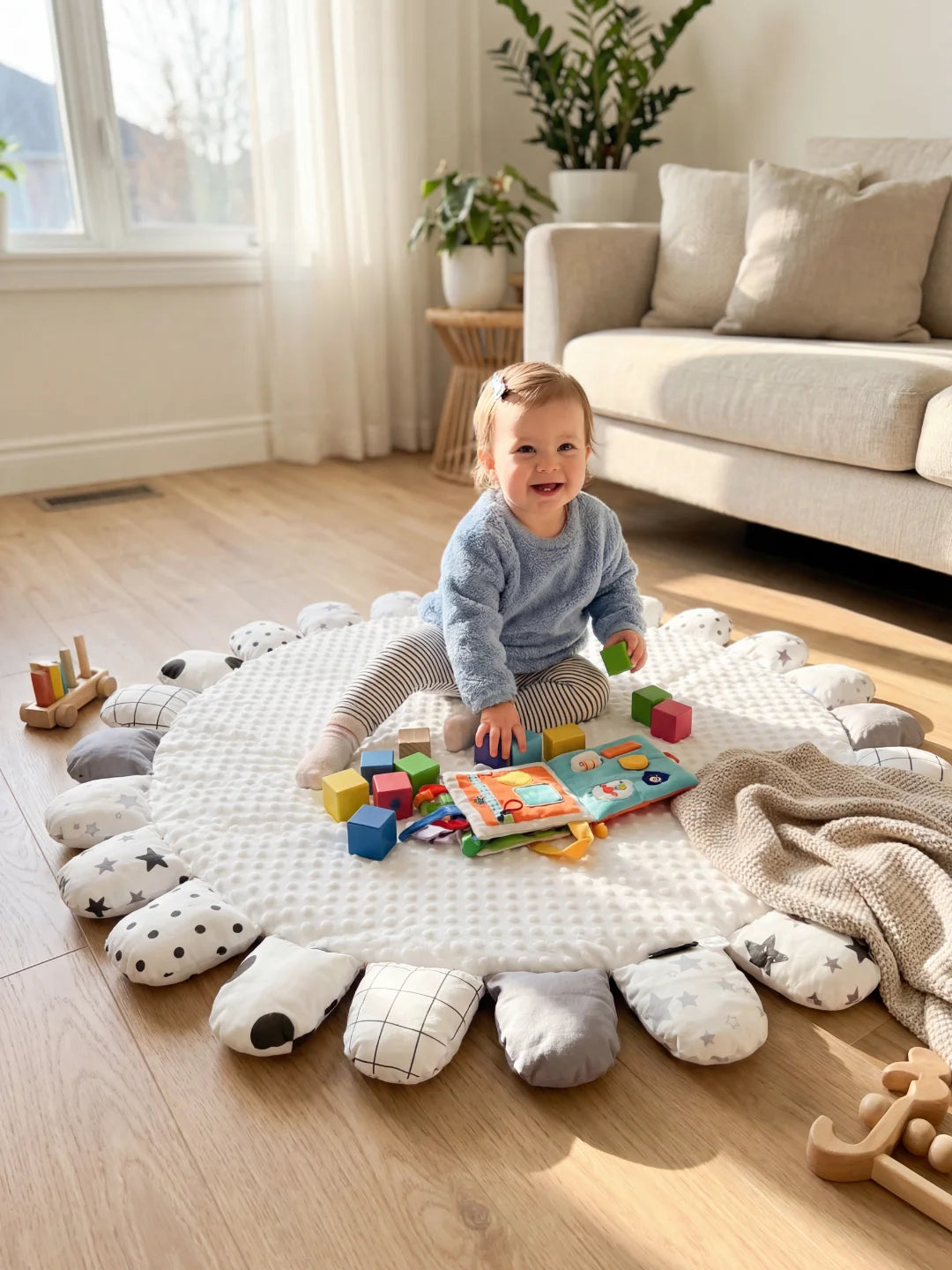 Enfant assise sur un tapis d'éveil blanc minky jouant avec des cubes colorés et un livre d'activités tactile.
