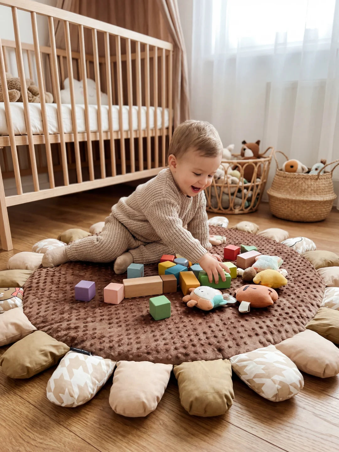 Enfant assis sur un tapis de sol à pétales manipulant des jouets en bois et des cubes souples dans un espace de jeu sécurisé.