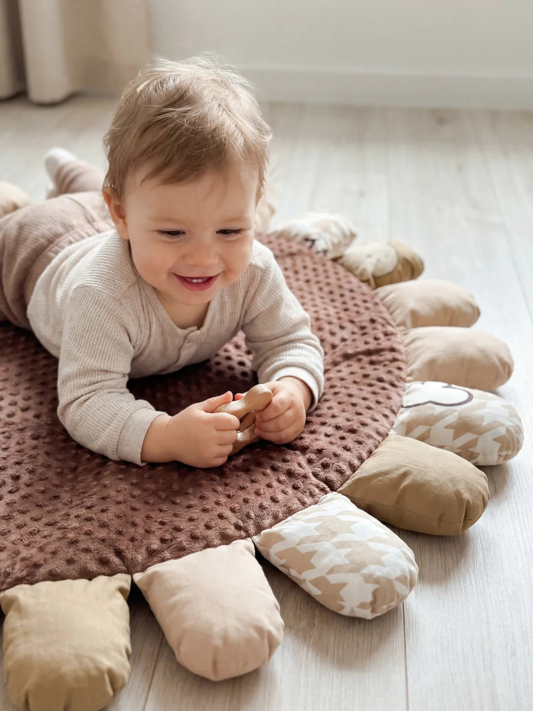 Bébé allongé sur le ventre sur un tapis minky marron, pratiquant la motricité libre avec un anneau de dentition en bois.