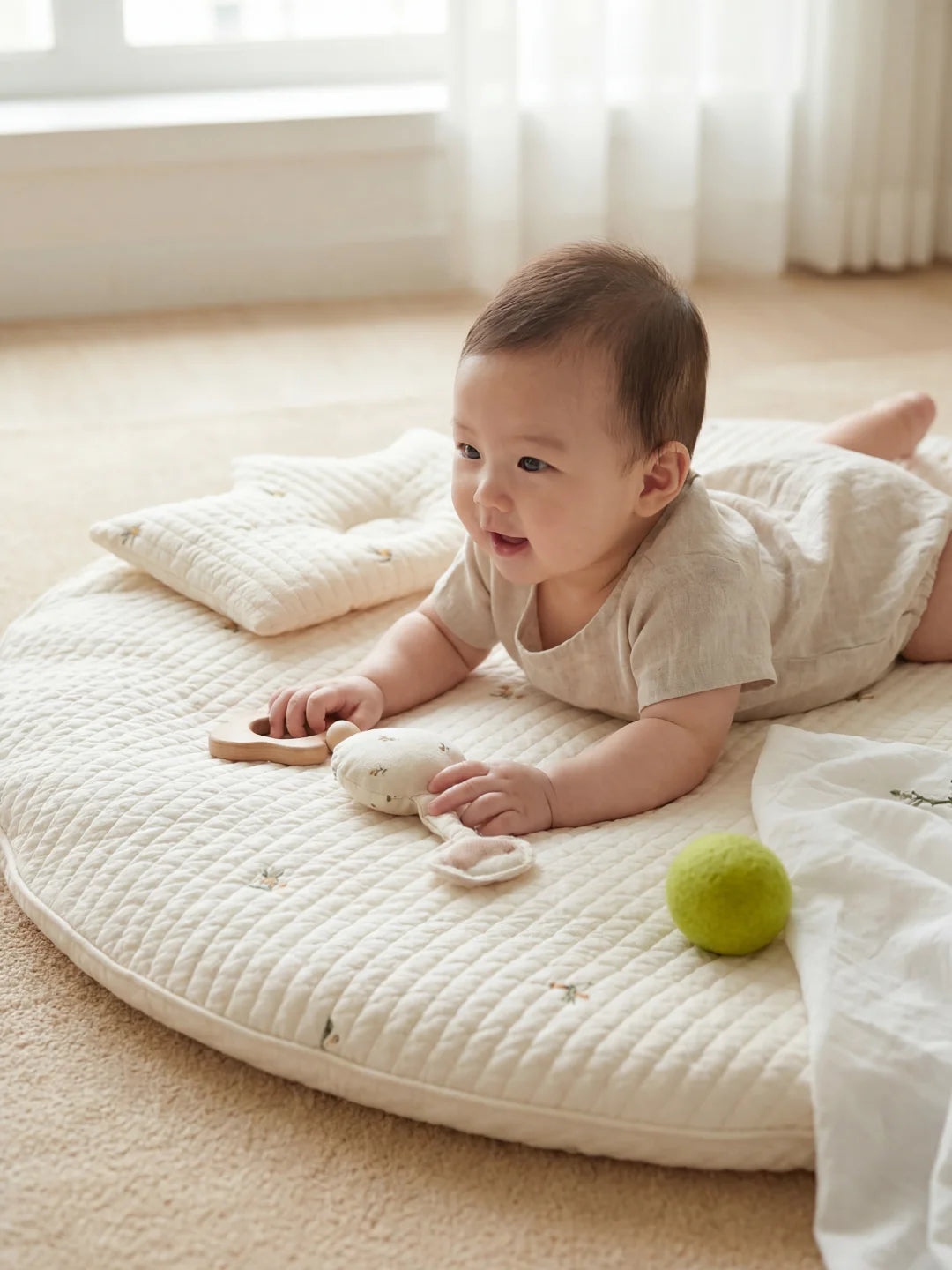 Bébé allongé sur le ventre sur un tapis d'activité blanc, s'amusant avec un hochet de dentition.
