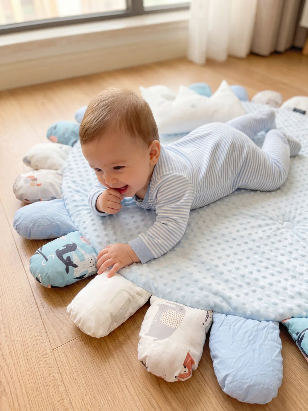 Bébé allongé sur le ventre sur un tapis d'éveil bleu ciel, explorant les textures et les motifs des pétales pour sa motricité.