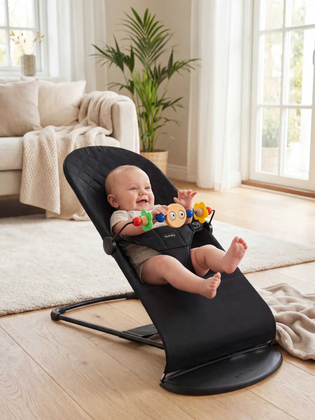 Bébé heureux s'amusant dans son transat noir ergonomique avec une arche de jouets rotative devant lui.