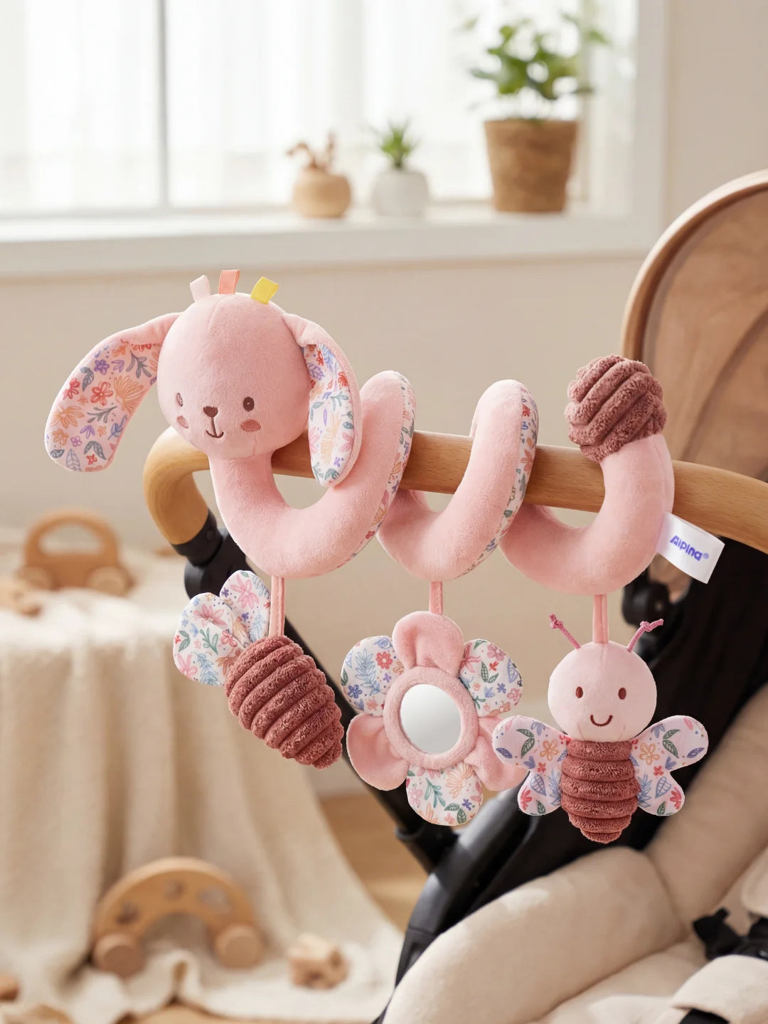 Jouet de poussette lapin rose en peluche douce installé sur un arceau de poussette en bois.