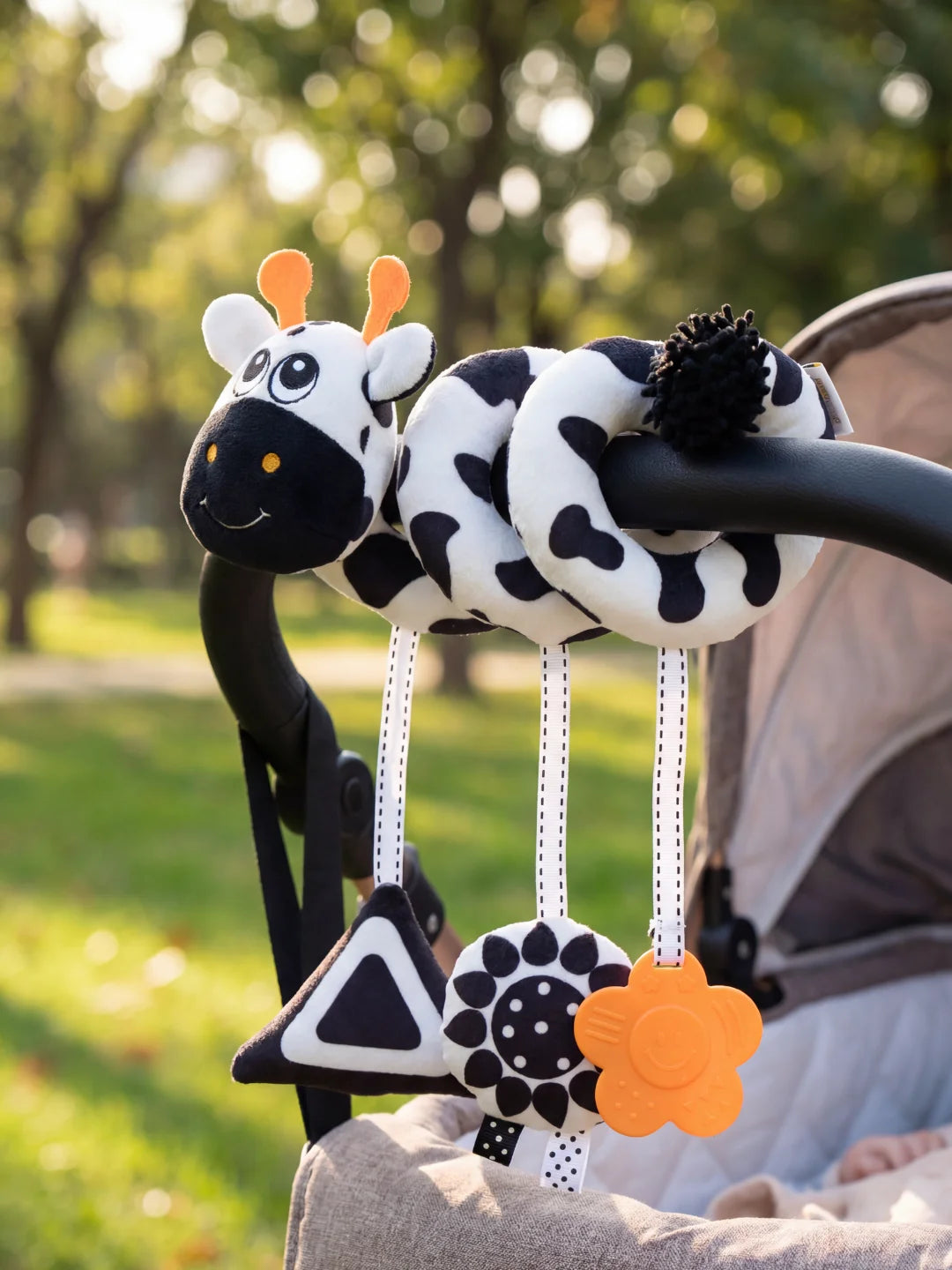 Chaîne de poussette contrastée noir et blanc avec hochet triangle et fleur de dentition orange.