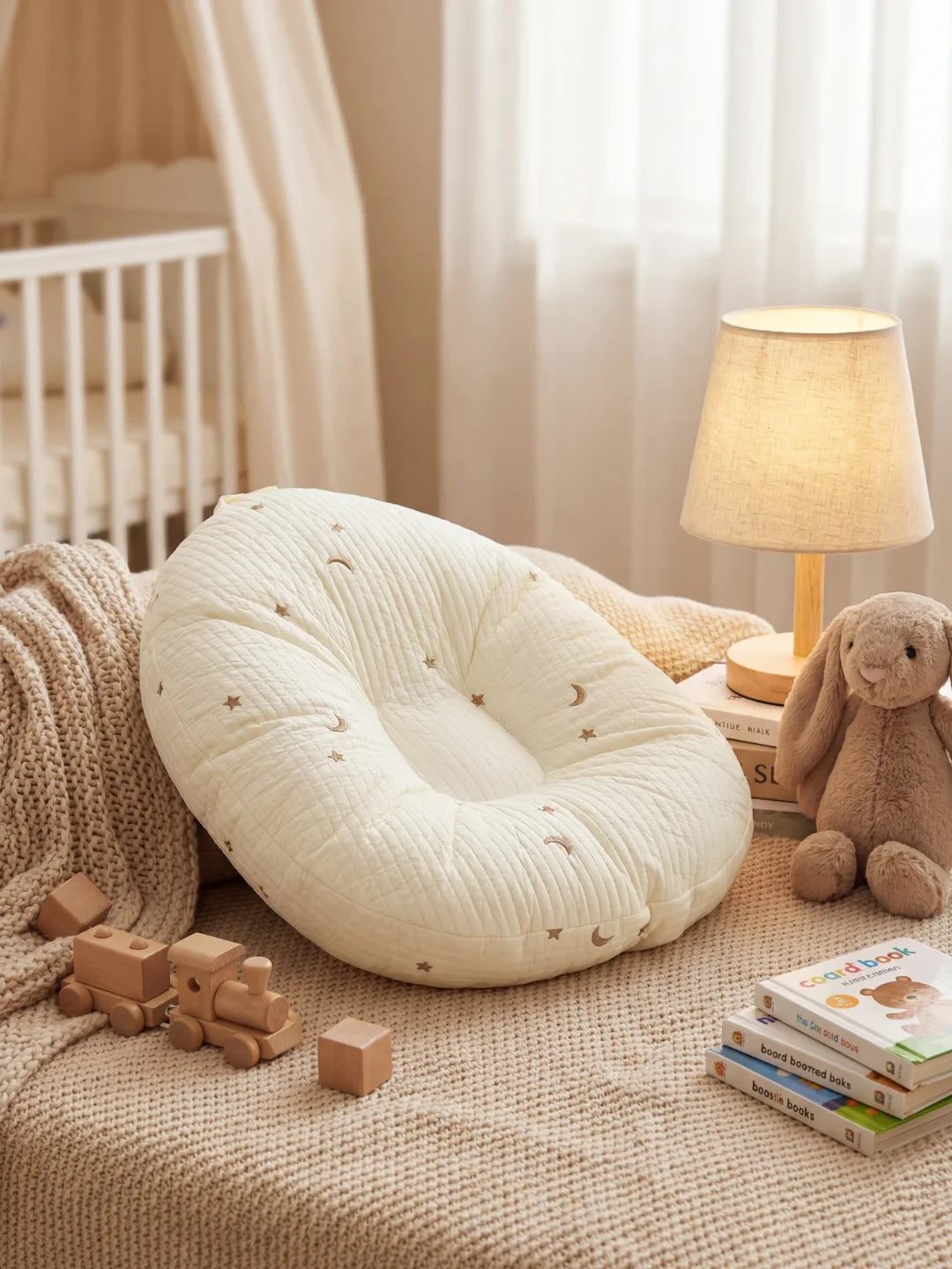 Coussin d'allaitement écru brodé étoiles posé dans une chambre de bébé