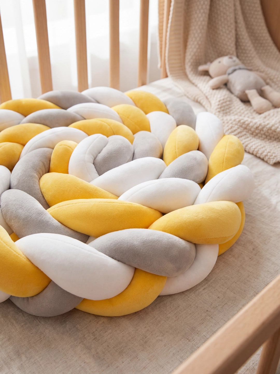 Coussin tressé décoratif jaune et gris posé dans un lit bébé à barreaux pour le confort et le style.