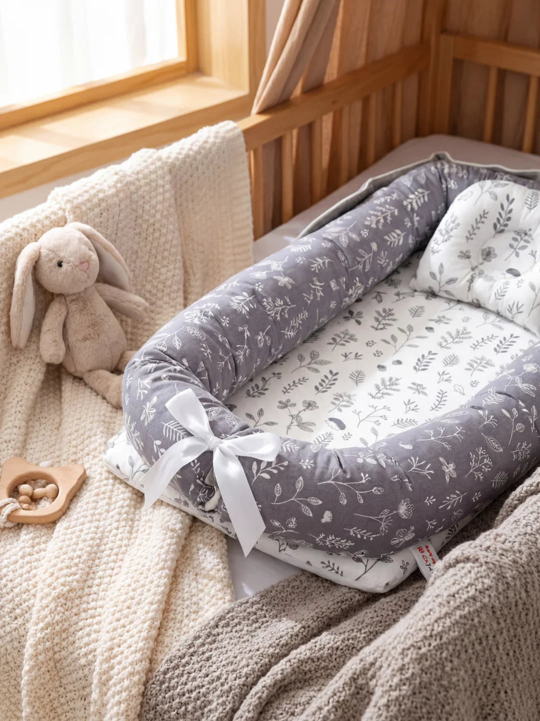 Détail du boudin et noeud blanc du réducteur de lit bébé gris motif feuillages dans un lit bébé