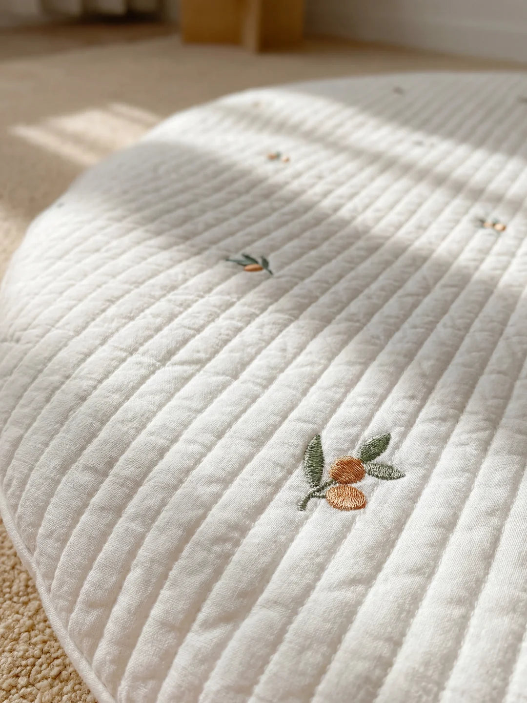 Gros plan sur une broderie délicate de branche d'olivier sur un tissu en coton matelassé blanc.