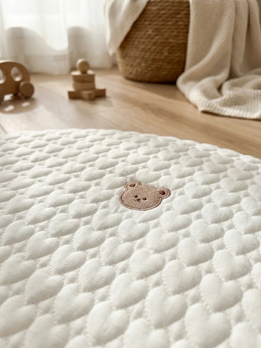 Détail de la broderie ours marron sur le tissu blanc texturé de cœurs d'un tapis d'éveil pour bébé.