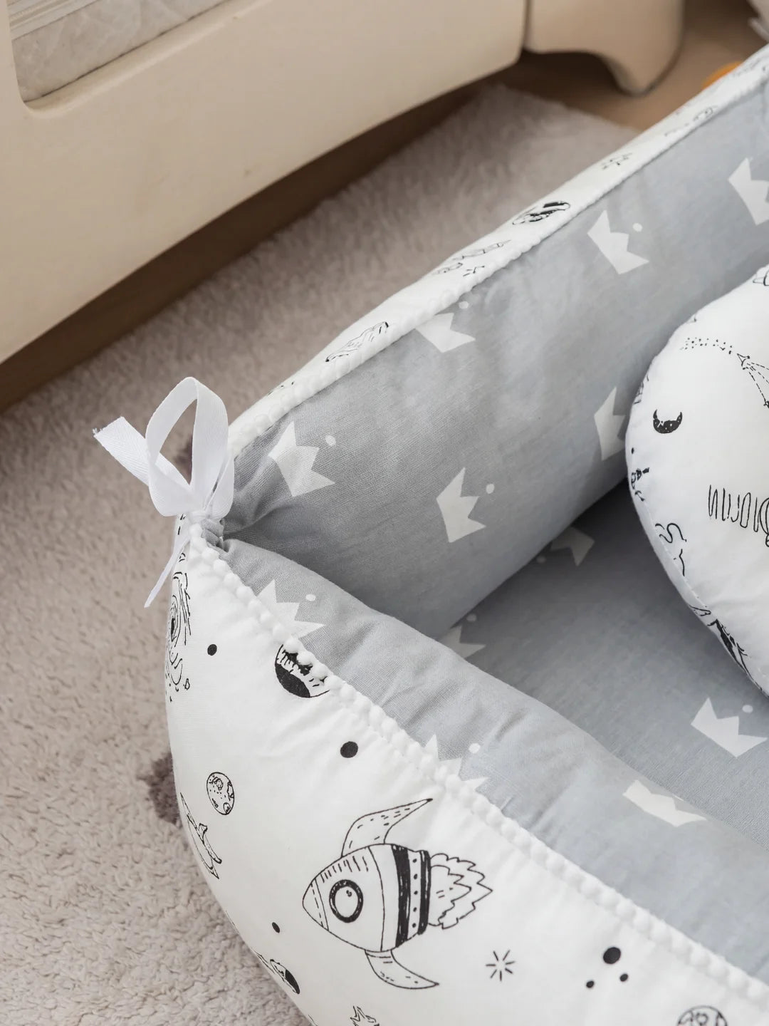 Zoom sur le nœud de serrage et les motifs de fusées spatiales d'un nid bébé en coton gris.