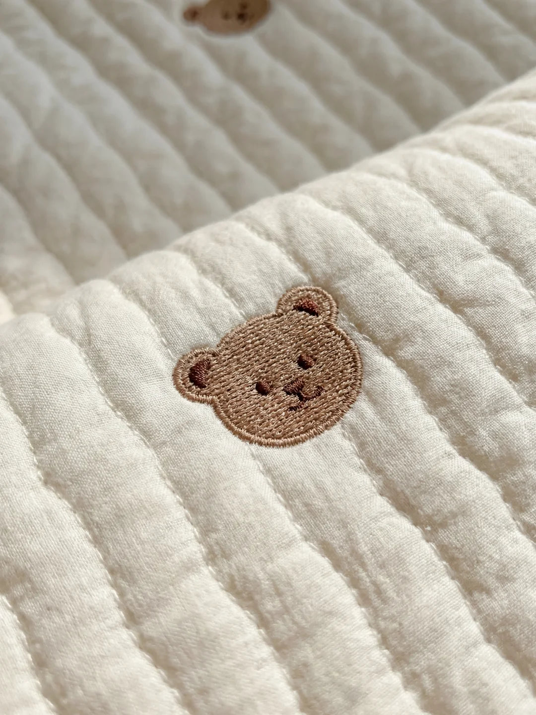 Gros plan sur les finitions et la qualité de la broderie "ours" d'un tapis d'éveil pour nouveau-né.
