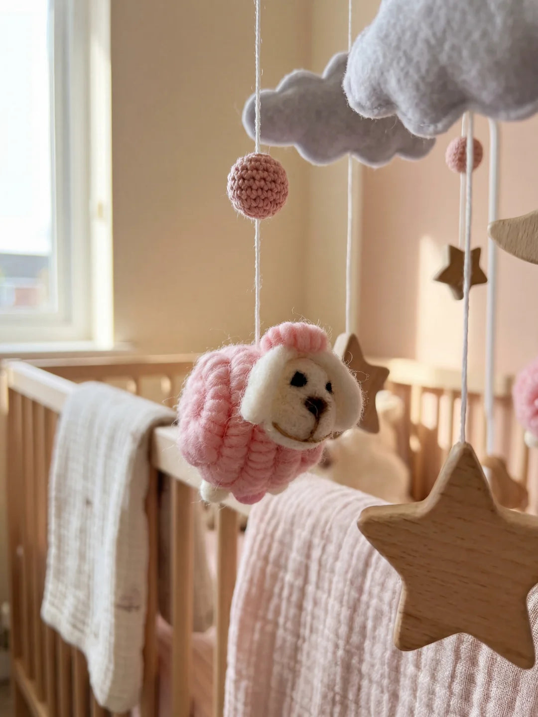 Gros plan sur un mouton en laine rose bouclée et une étoile en bois naturel sur un mobile bébé.