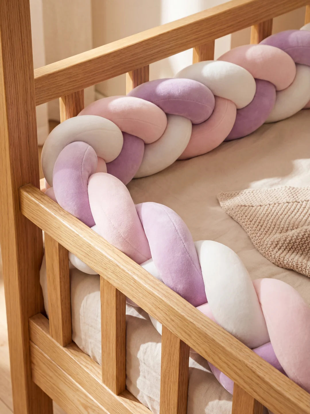 Détail de la protection en tresse de lit rose et violette fixée contre les barreaux en bois du lit.