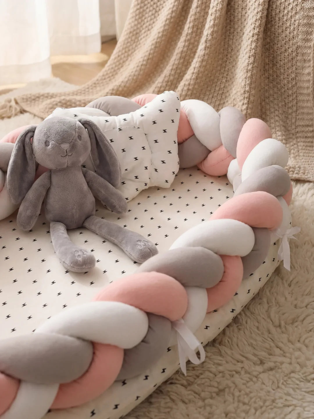 Détail du réducteur de lit tressé rose gris et blanc avec peluche lapin