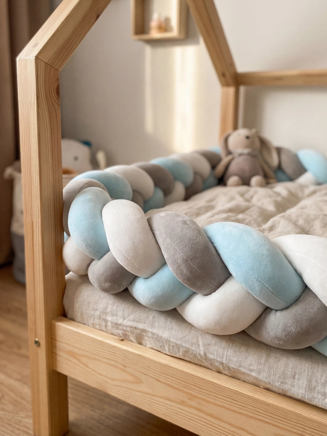 Zoom sur l'angle d'un lit en bois montrant le moelleux d'un tour de lit tressé bleu pastel et blanc.