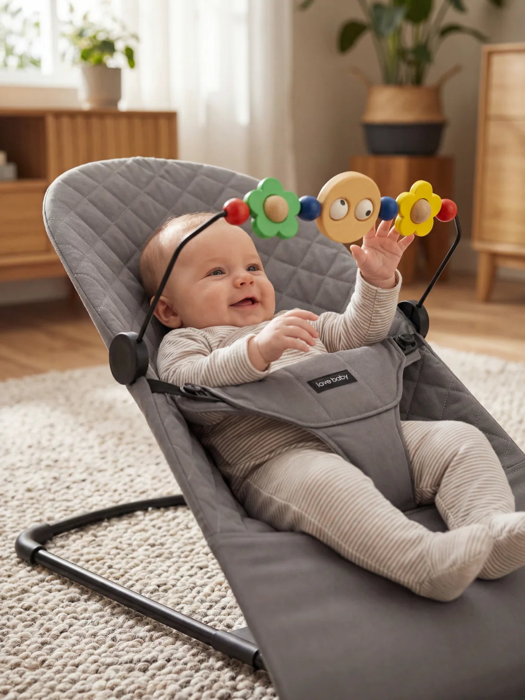 Bébé tendant les mains vers les jouets colorés de l'arche fixée sur son transat gris.