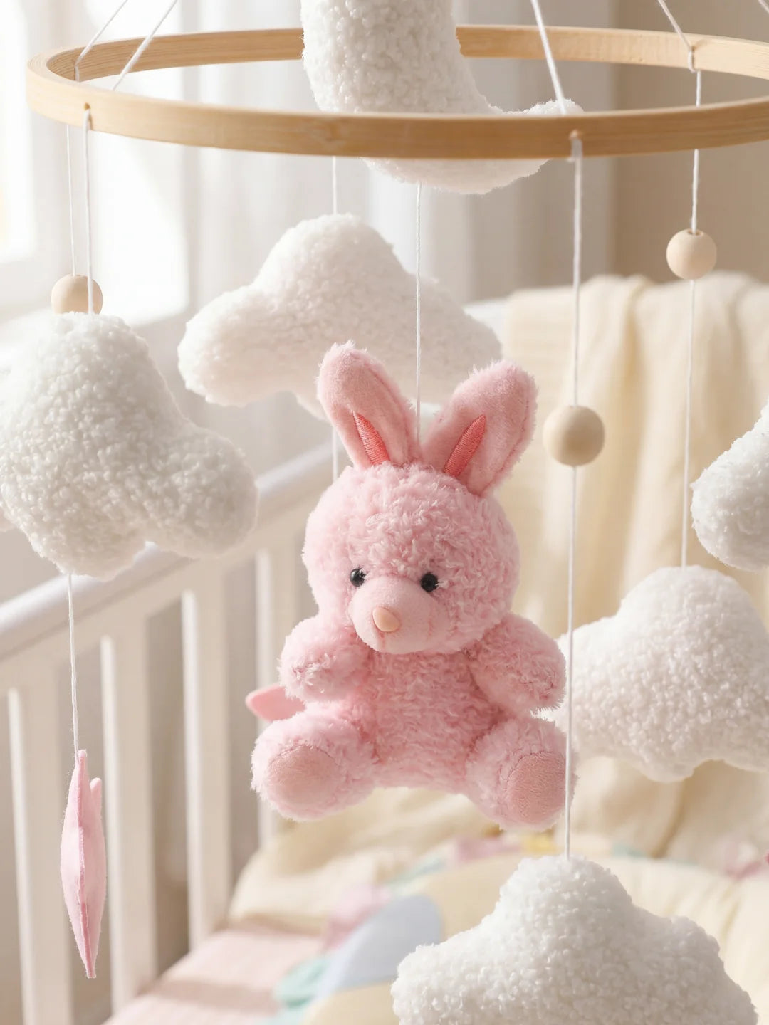 Gros plan sur les finitions d'un mobile : nuages en laine bouclée et lapin rose en peluche.