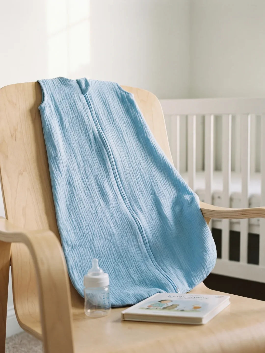 Gigoteuse bébé gaze de coton bleu jean posée sur fauteuil avec biberon dans chambre