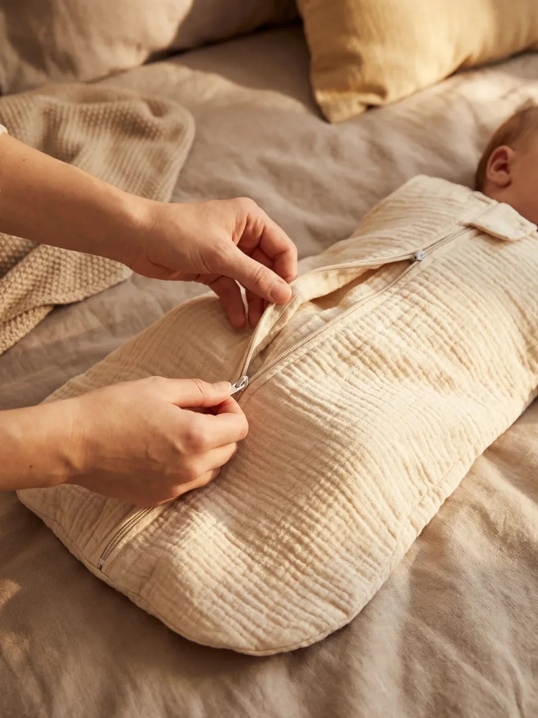 Parent ouvrant la fermeture éclair de la gigoteuse gaze de coton écru sur bébé