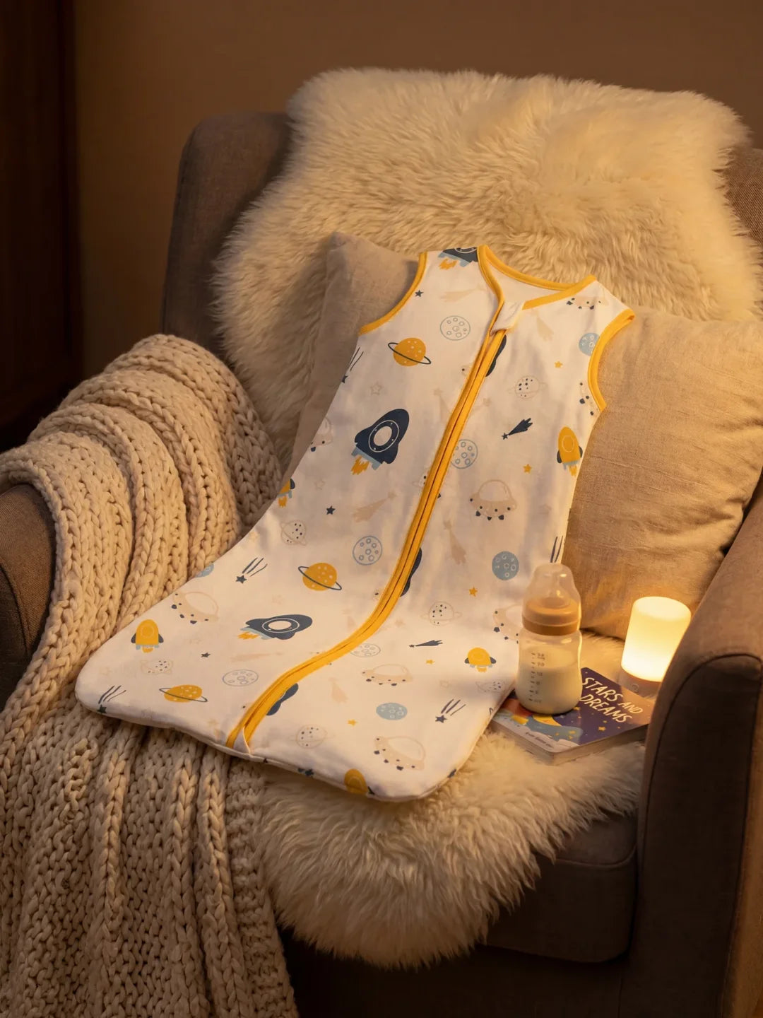 Gigoteuse bébé motif espace fusées posée sur fauteuil avec biberon et veilleuse