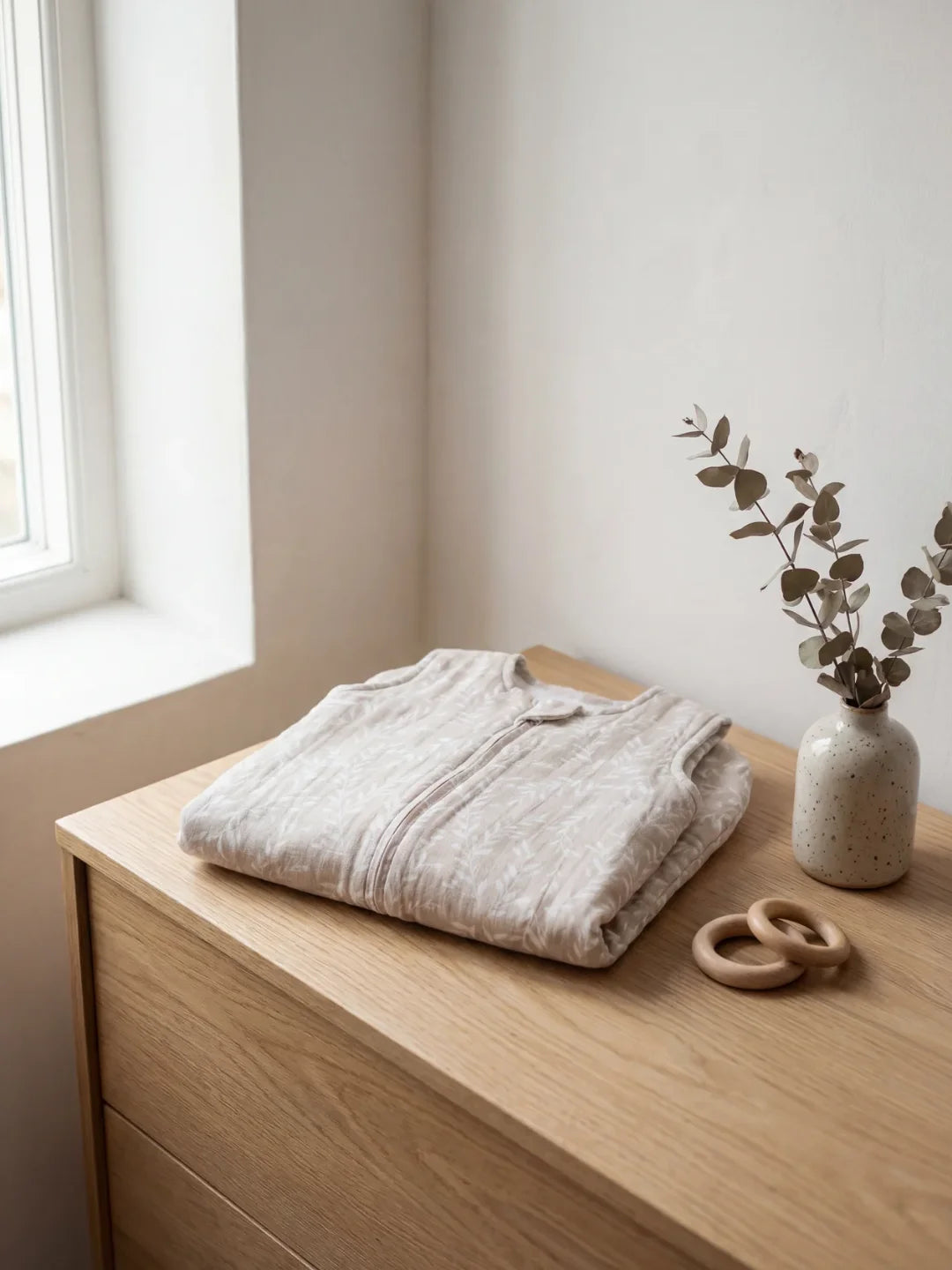 Gigoteuse bébé en mousseline beige pliée sur une commode en bois naturel