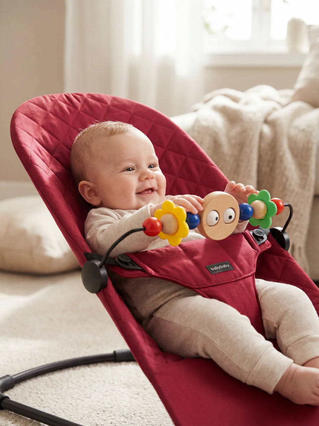 Détail d'un bébé manipulant les jouets en bois de l'arche installée sur son transat matelassé bordeaux.