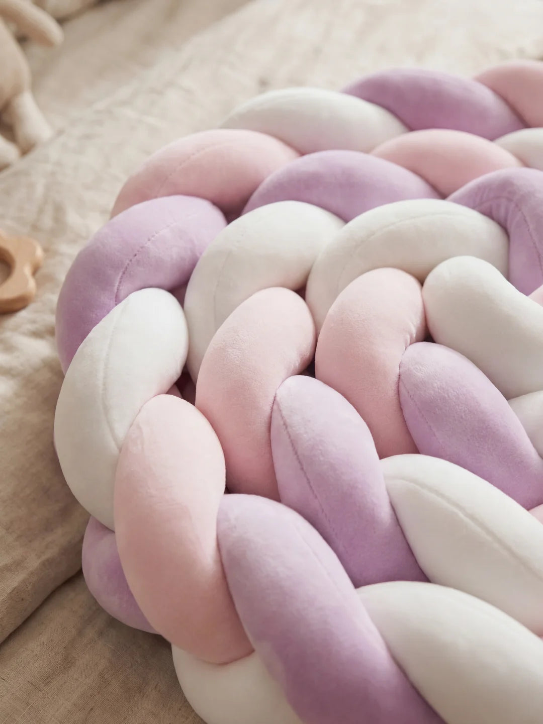 Zoom sur le tressage en velours d'un coussin décoratif aux teintes mauve, rose et blanc.