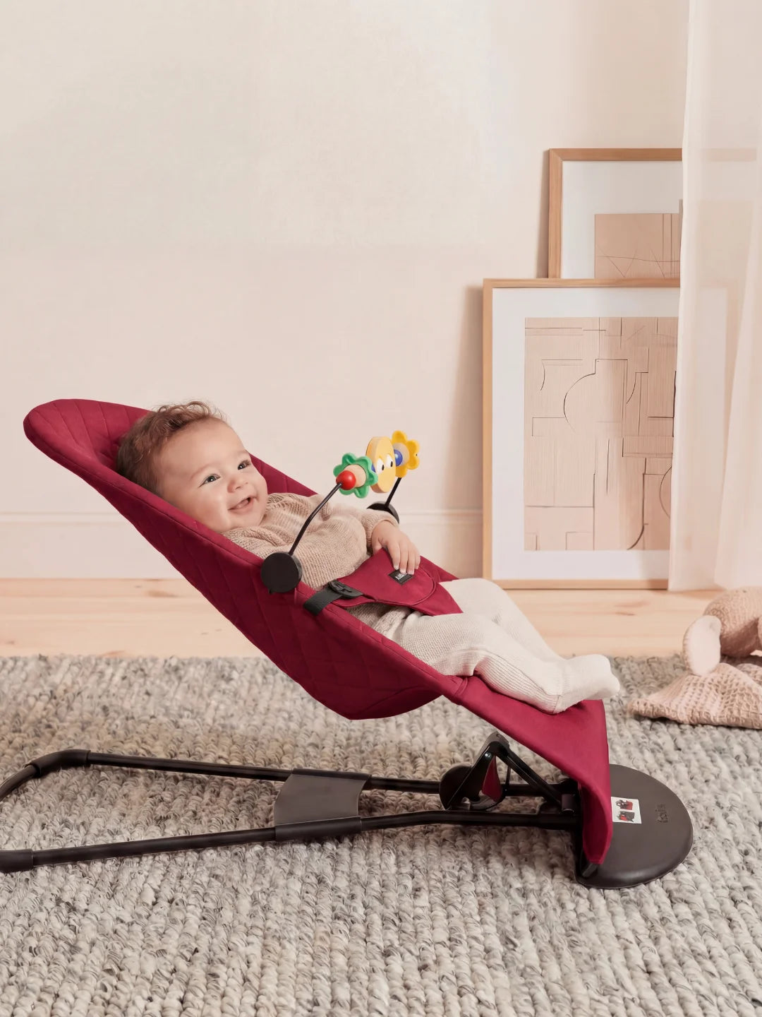 Vue de profil d'un bébé installé dans son transat bordeaux, montrant l'inclinaison idéale pour le maintien du dos.