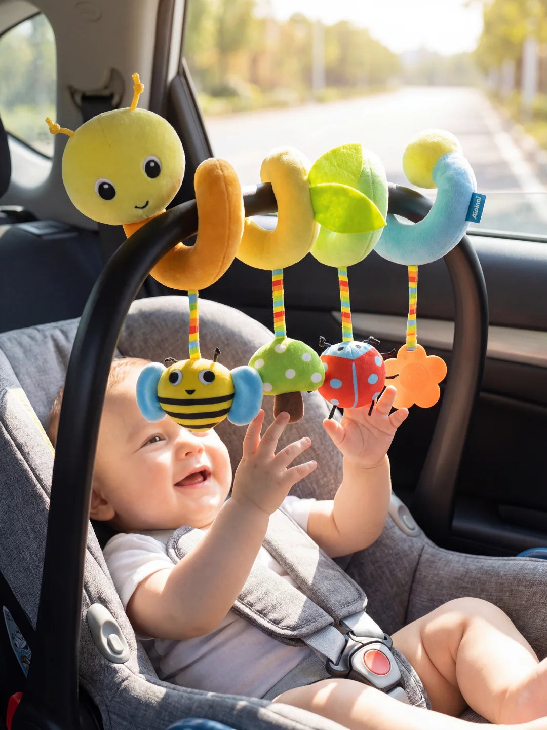 Bébé souriant dans son siège auto jouant avec la spirale d'activité chenille et ses insectes.