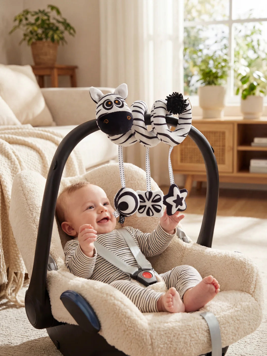 Bébé souriant dans son siège auto jouant avec la spirale zèbre et ses hochets suspendus.