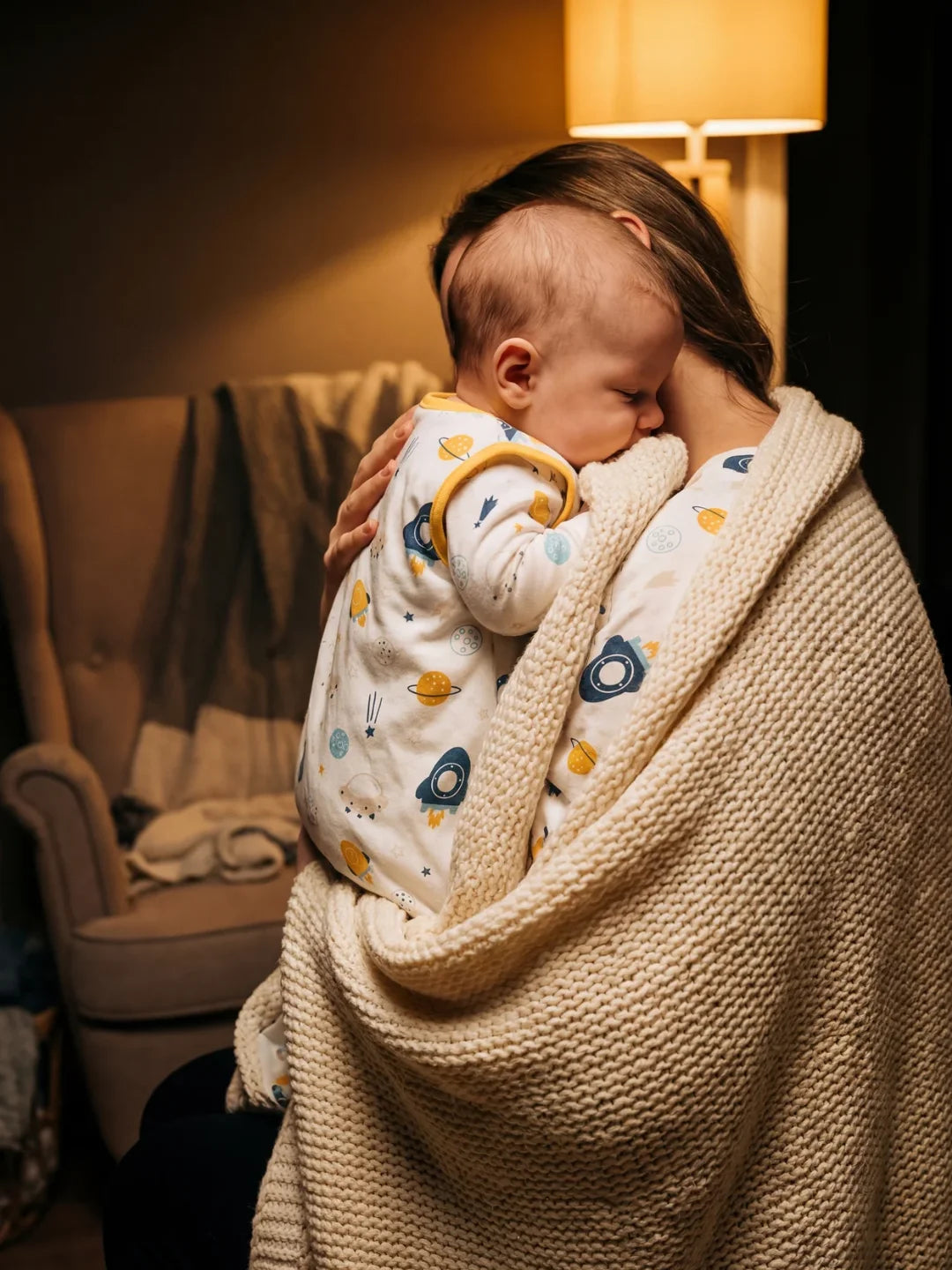 Maman portant bébé endormi dans sa gigoteuse motif espace fusées le soir