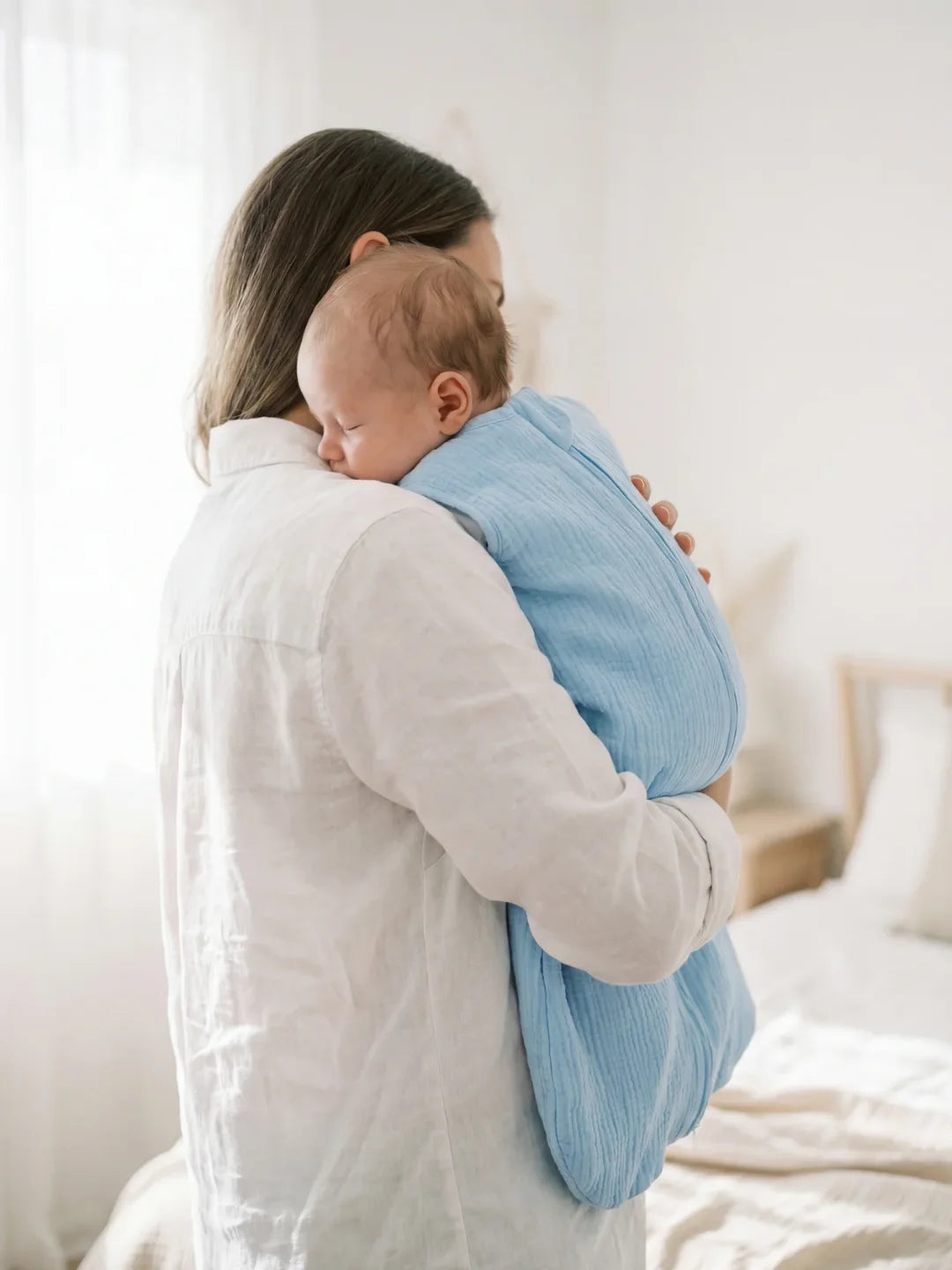 Maman portant bébé endormi dans sa gigoteuse gaze de coton bleu ciel dans chambre