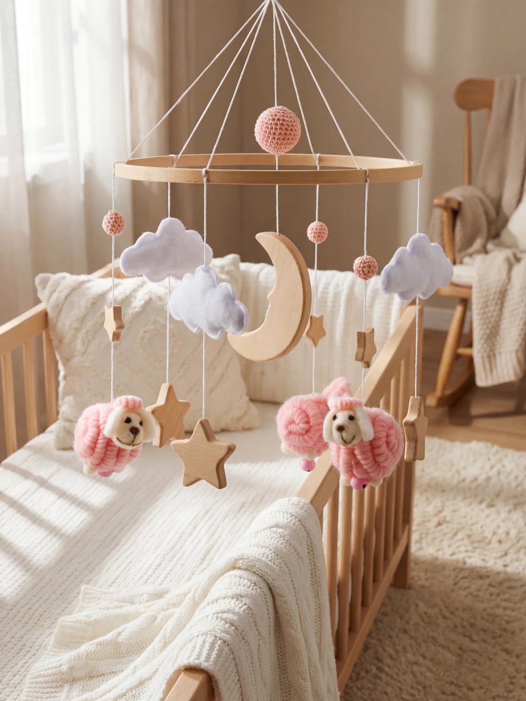 Mobile bébé artisanal avec moutons en laine, étoiles en bois et pompons roses au-dessus du lit.