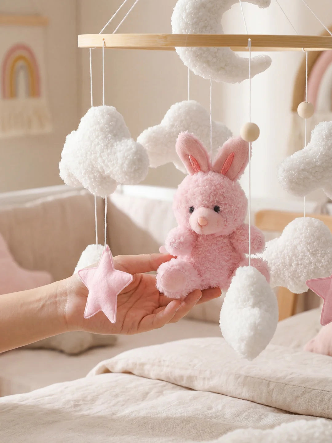 Main tenant délicatement la peluche lapin rose d'un mobile bébé pour montrer la douceur.